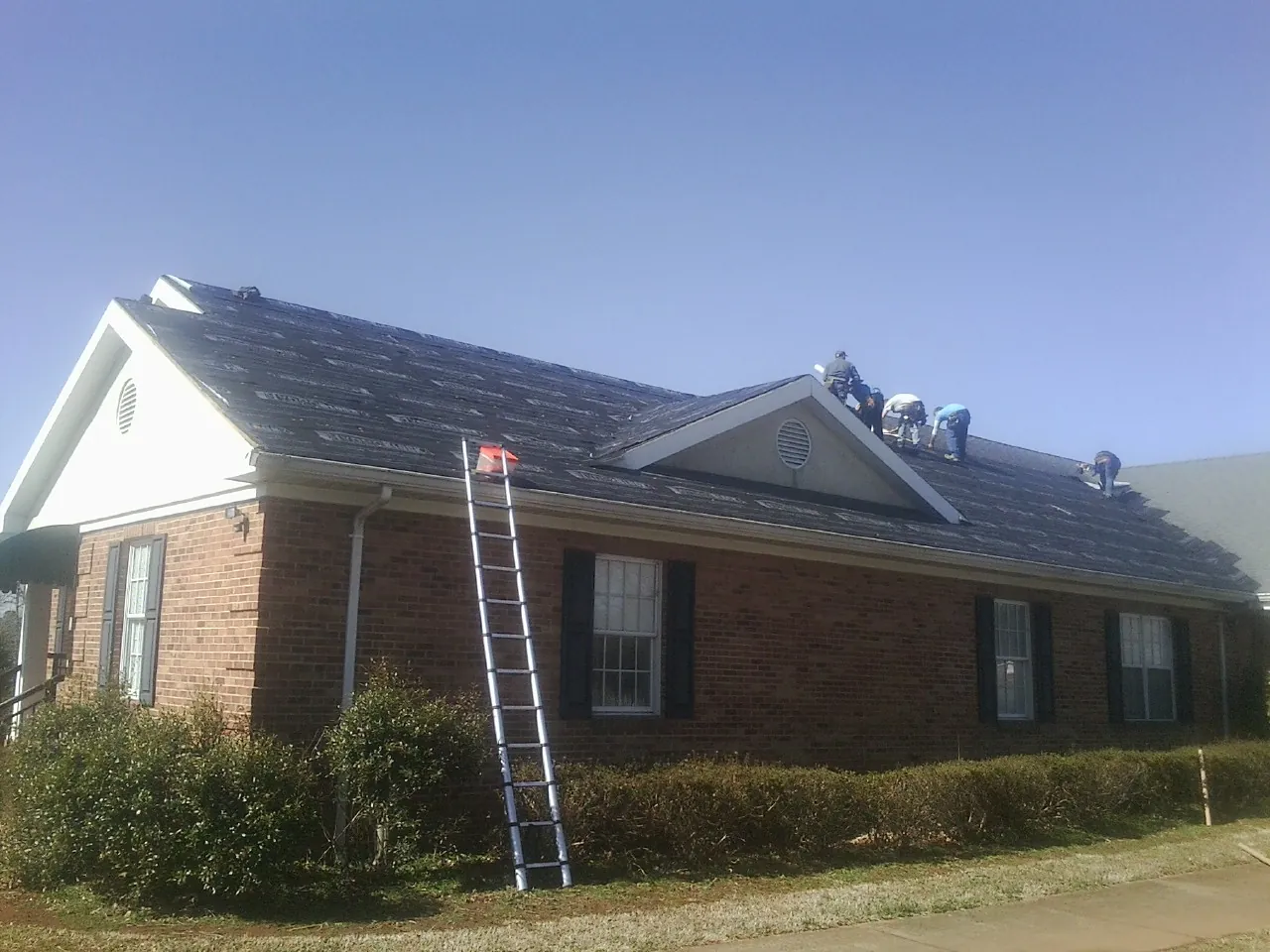 Crew tearing shingles off a brick ranch roof with a ladder set — Metal Roof Repair work by our crew in Oaklyn
