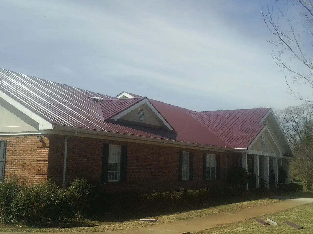 Red metal roof with gabled entries on a long brick building, from a Hail Damage Roof Repair job in Oaklyn