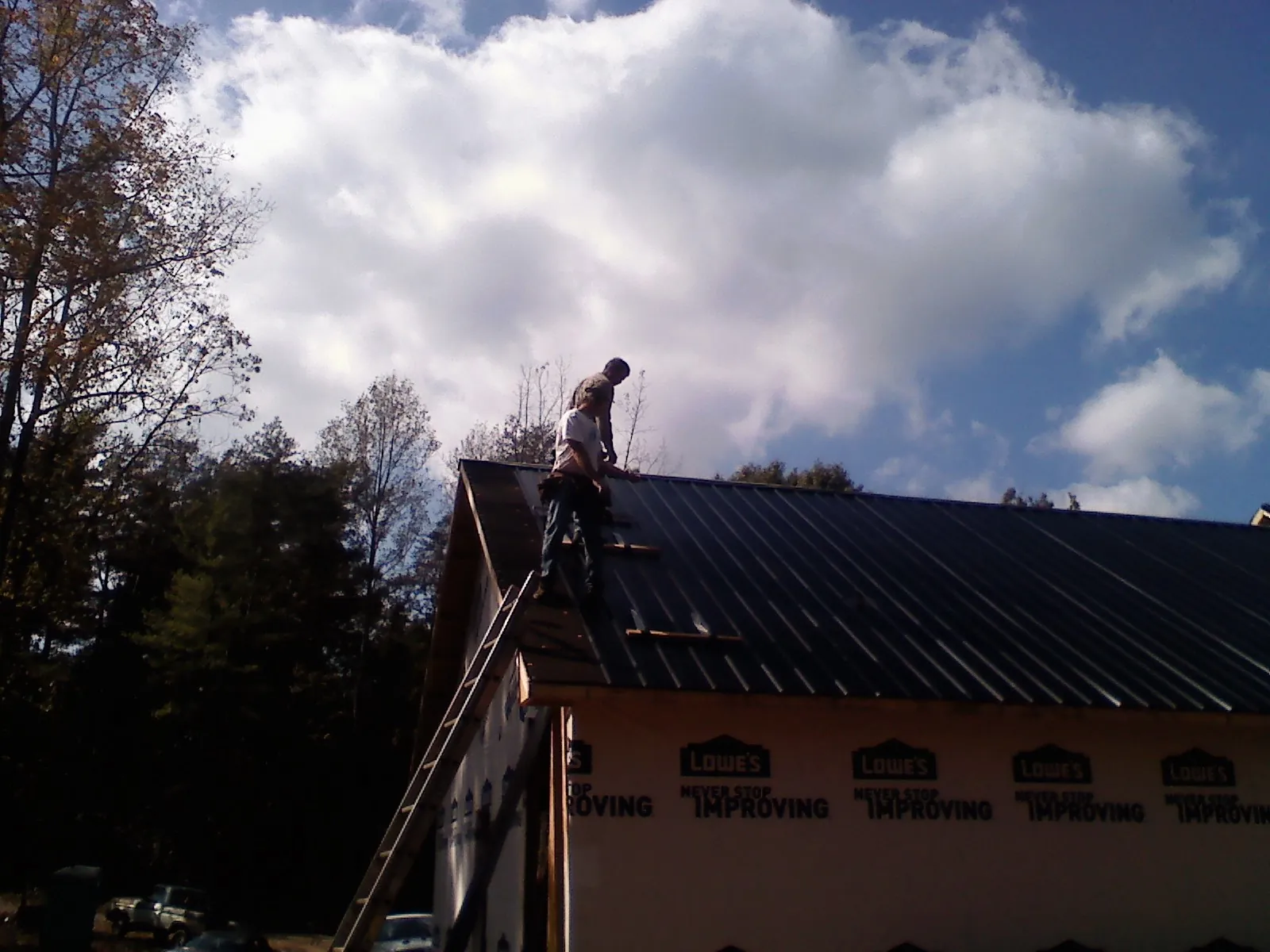 Roofer fastening dark metal panels high against a cloudy sky, from a Roof Inspection job in Oaklyn