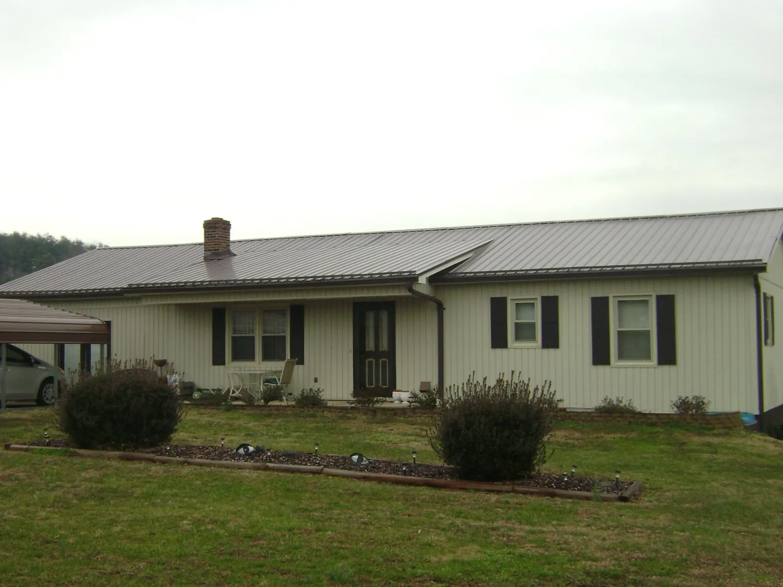 Brown metal roof on a cream sided ranch home with a brick chimney in Oaklyn
