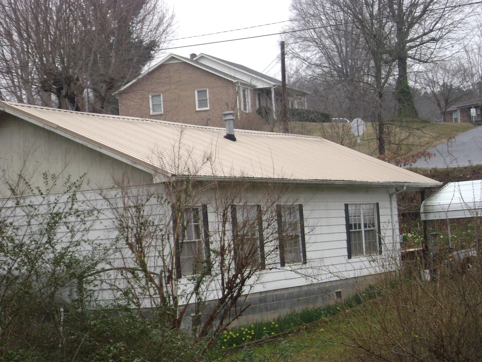Tan metal roof on a white sided house set into a hillside — Commercial Roofing by Roofing Brothers in Oaklyn